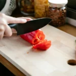 Close-up of slicing a red bell pepper on a wooden cutting board.