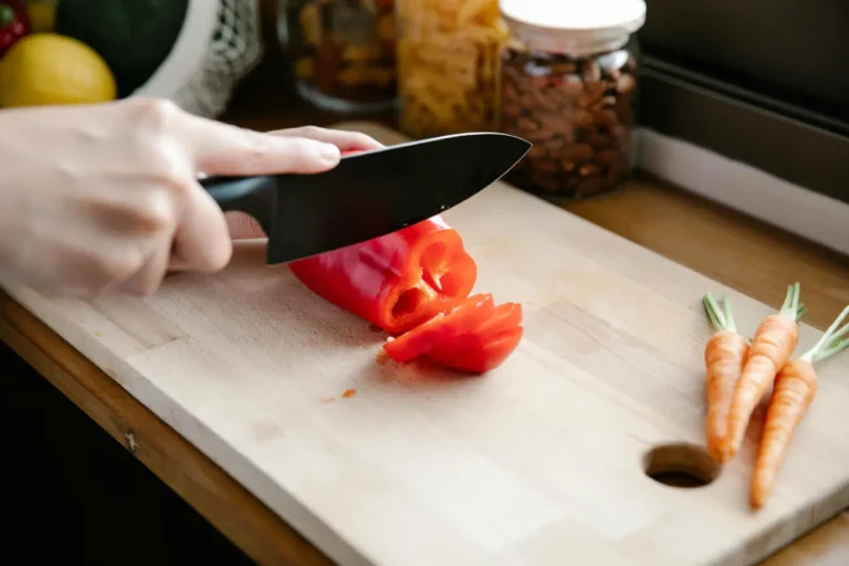 Close-up of slicing a red bell pepper on a wooden cutting board.